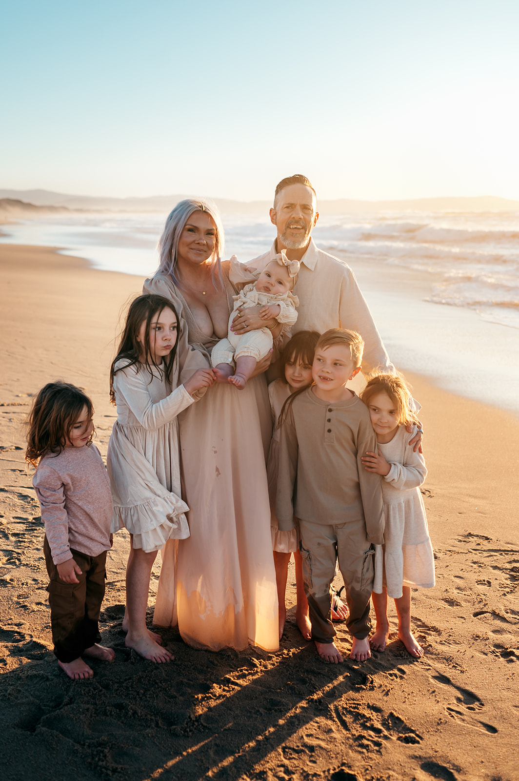 Family of eight in coordinated neutral outfits standing on the beach at golden hour on the Monterey coast