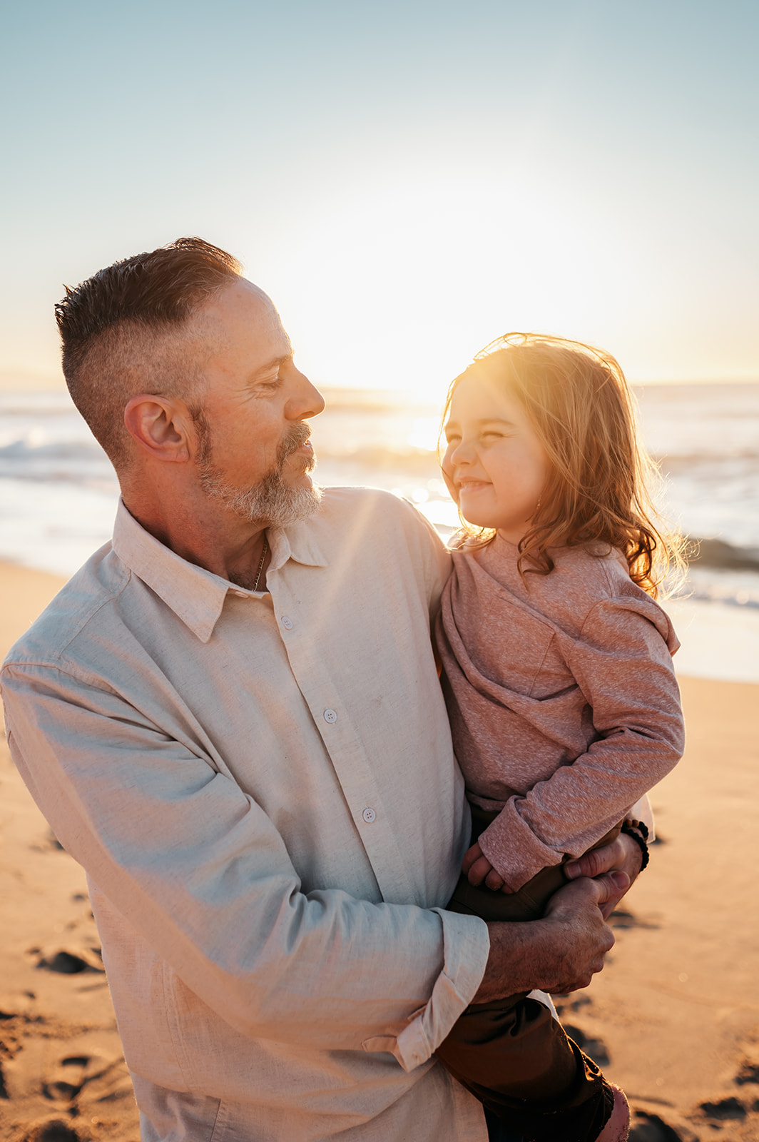Father holding his young son at the beach, both backlit by golden hour light on the Monterey coast