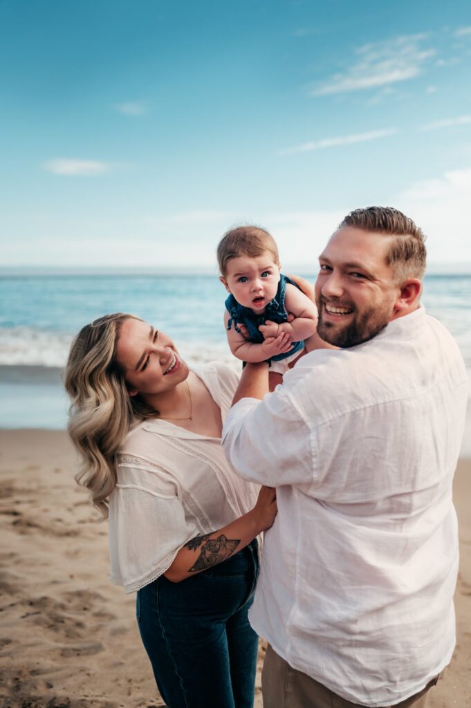 Parents holding their baby up toward the ocean at Moran Lake Park Beach on the East Side of Santa Cruz