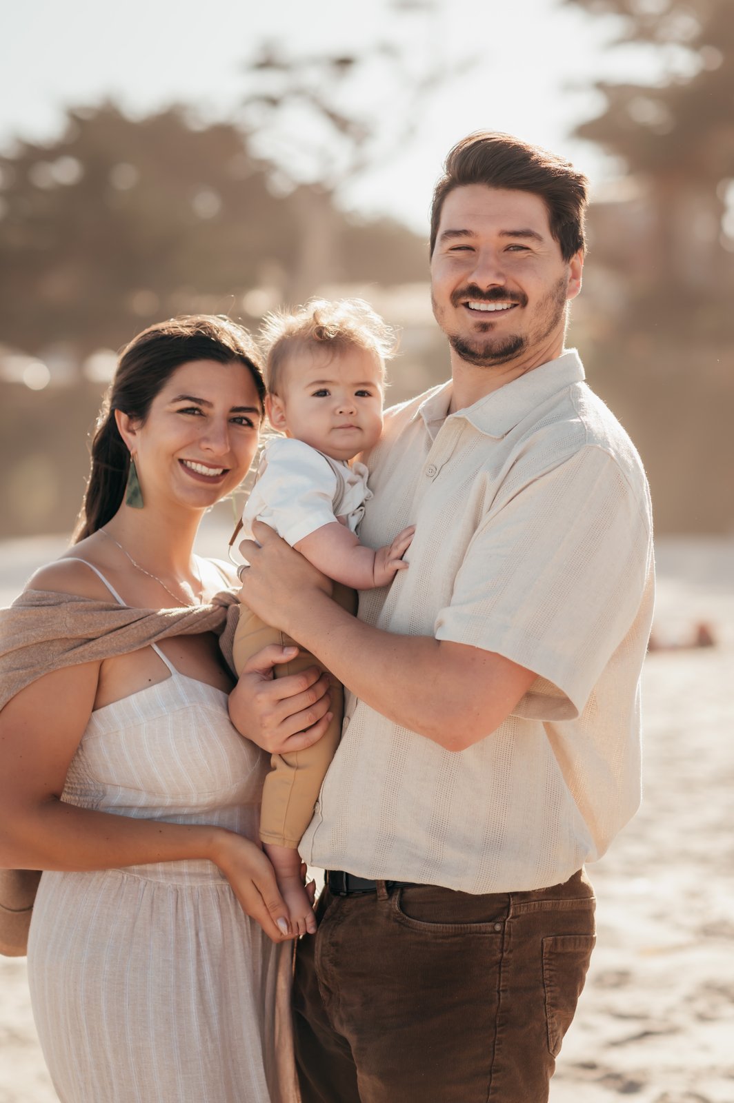 Family of three smiling on Carmel Beach during a golden morning family photography session