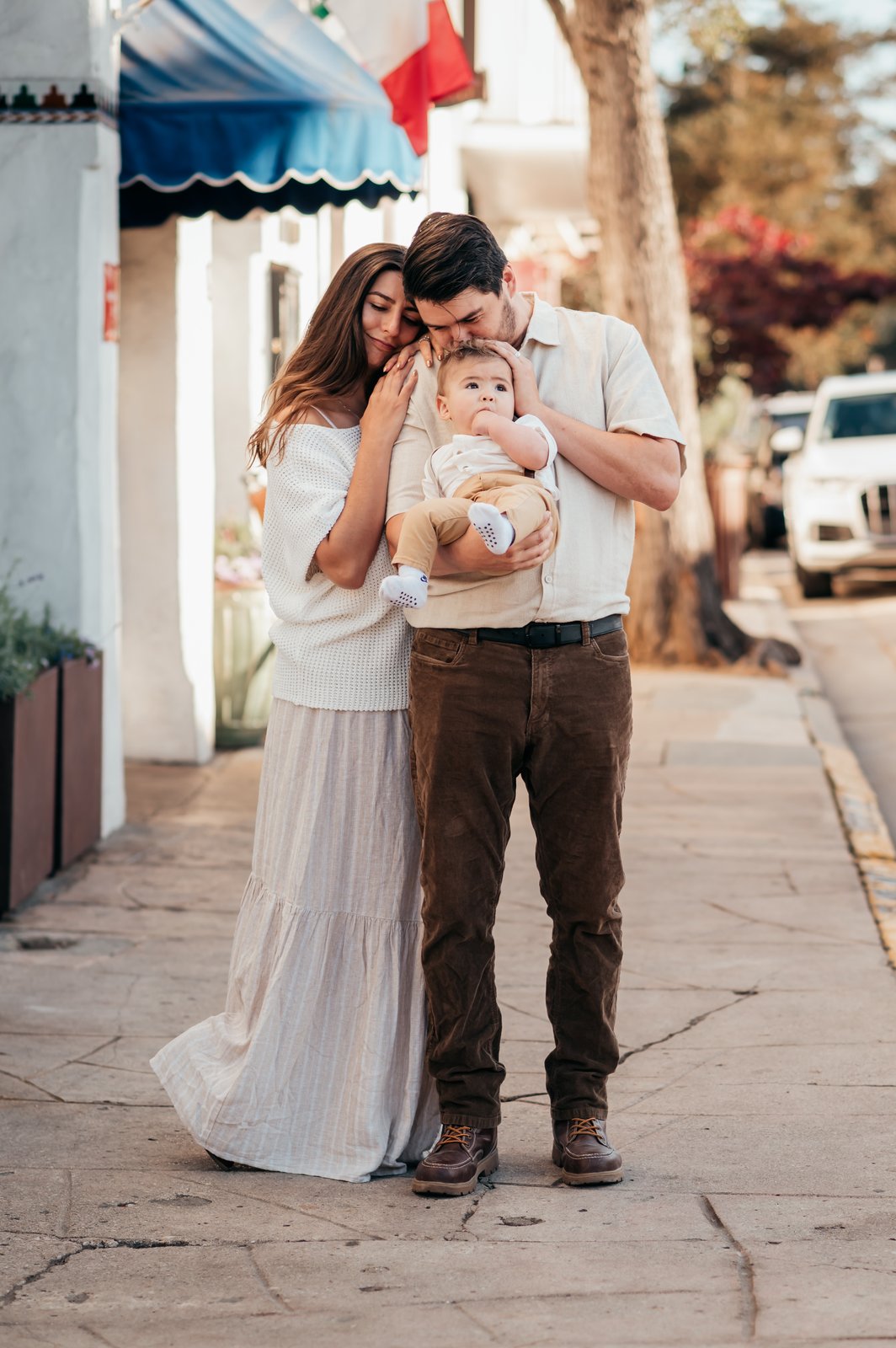Parents snuggling their baby on a quiet Carmel-by-the-Sea street with striped awnings