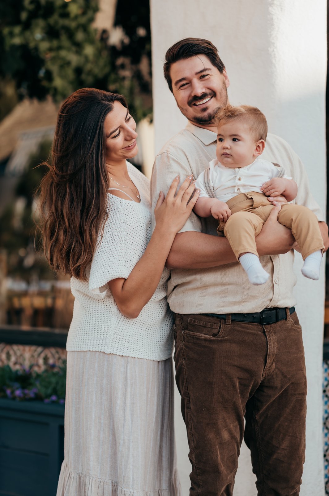 Mom smiling at baby boy held by dad in front of a Carmel-by-the-Sea storefront