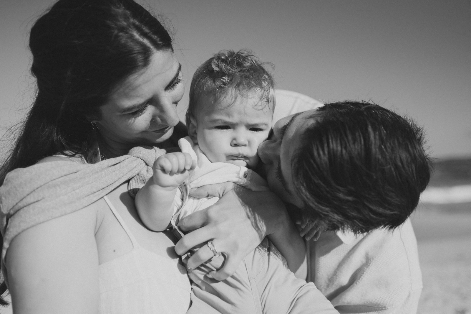 Black and white close-up of parents kissing their baby's cheeks at a Carmel family session