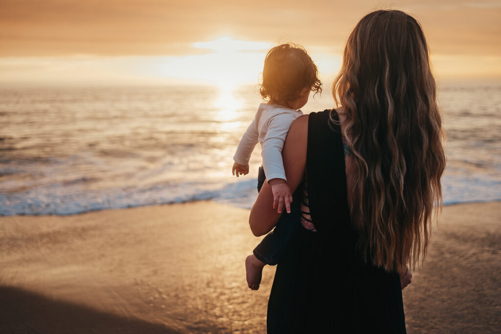 Mother holding her toddler at sunset on the beach at Fort Ord Dunes State Park in Marina, CA