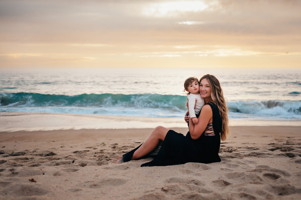 Mom smiling while snuggling her baby on the sands of Monterey Bay.
