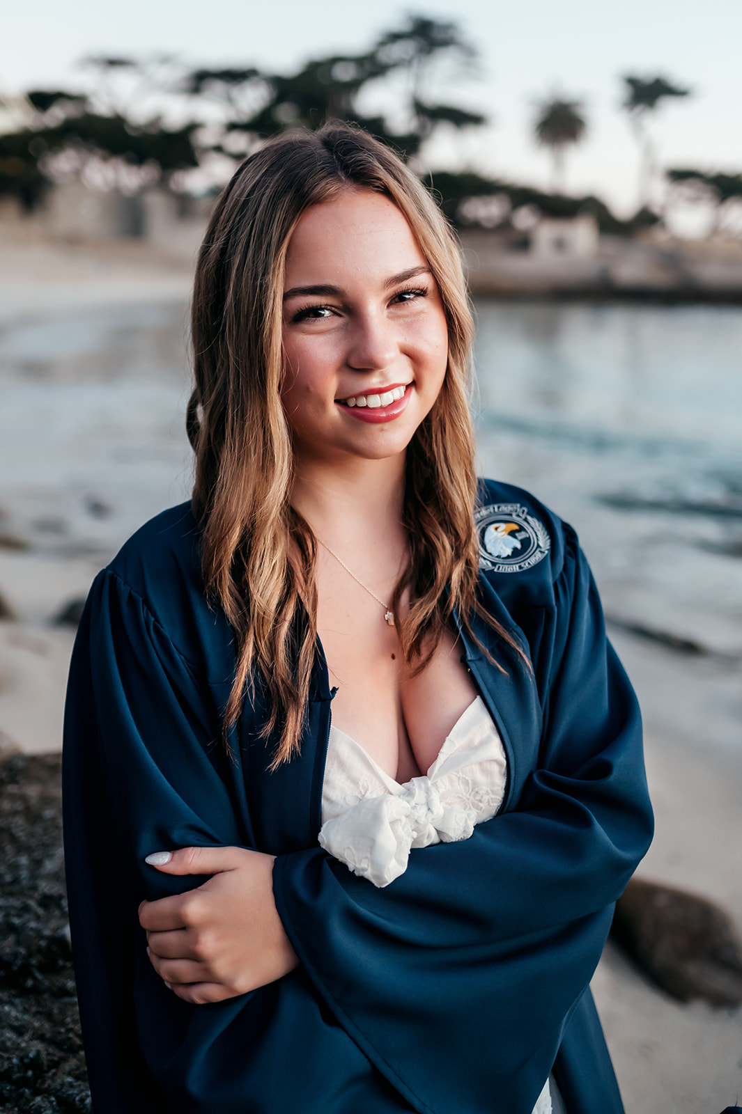 Smiling senior in her graduation gown with Lovers Point cove behind her in Pacific Grove
