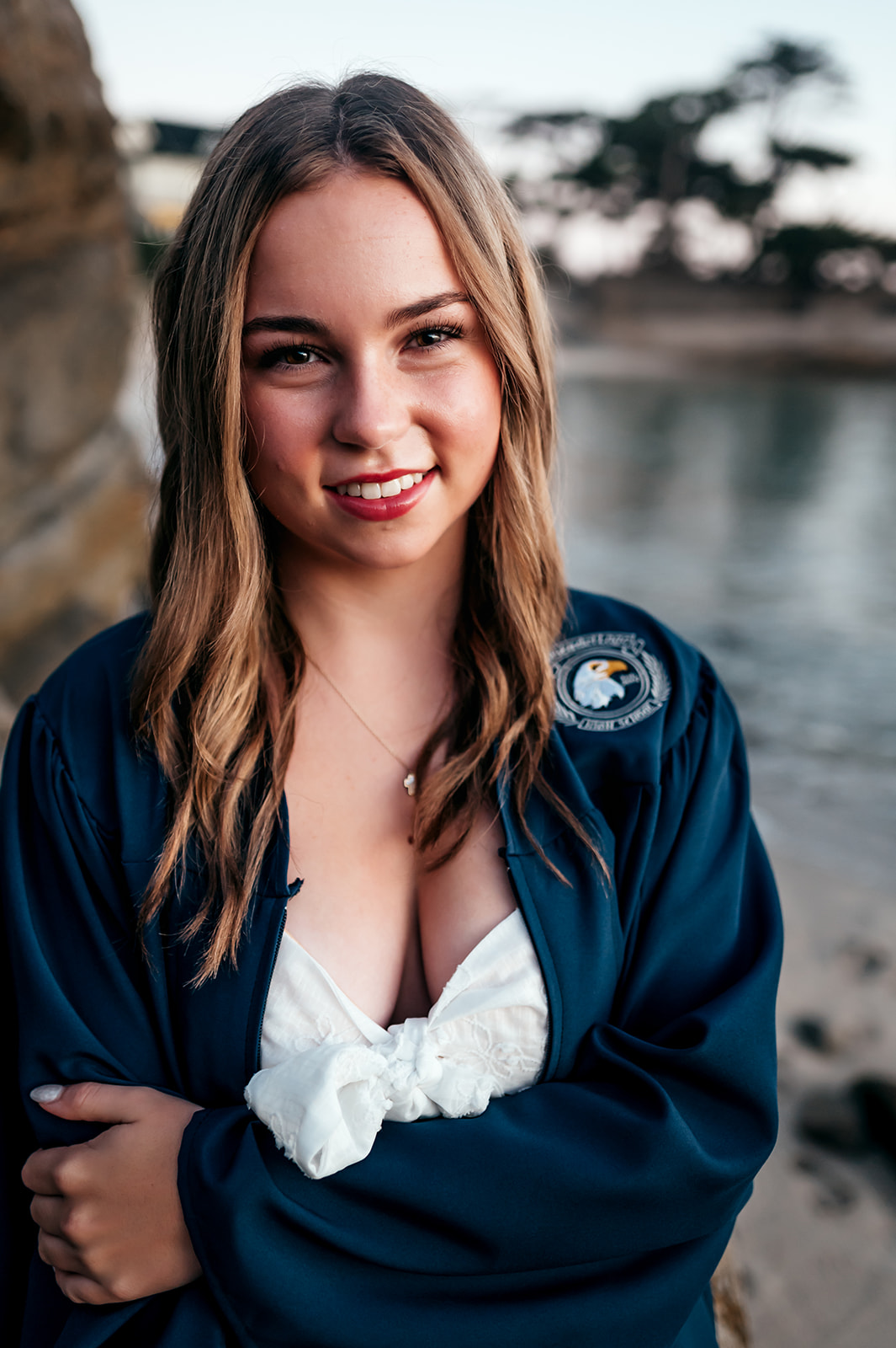 Senior smiling in her cap and gown at Lovers Point Beach in Pacific Grove