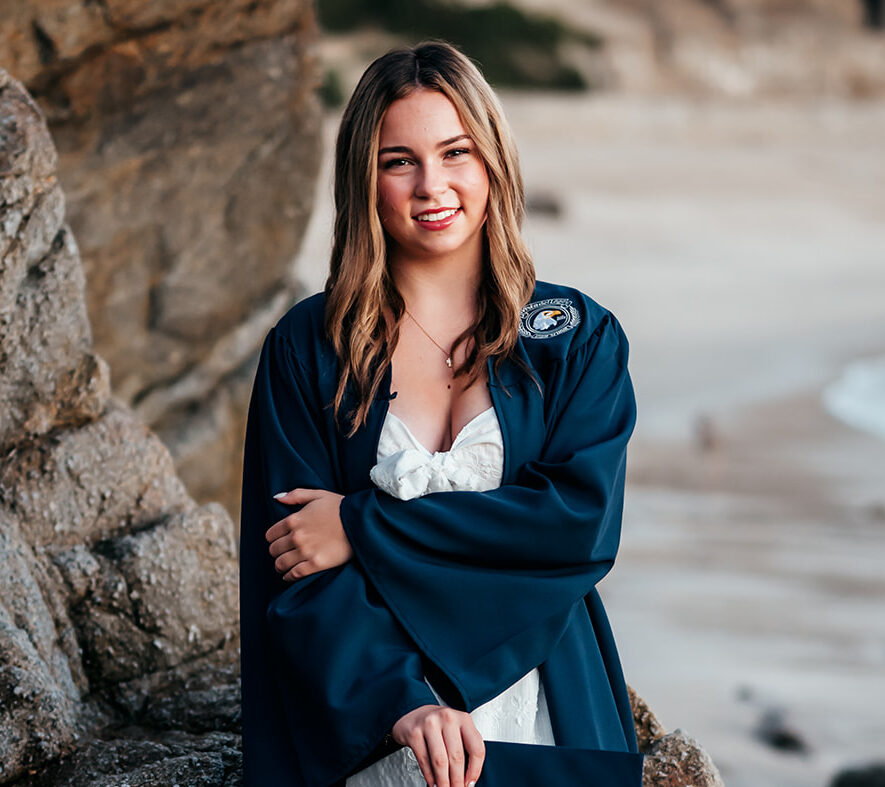 High school senior in cap and gown at a sunrise senior session at Lover's Point Beach in Pacific Grove