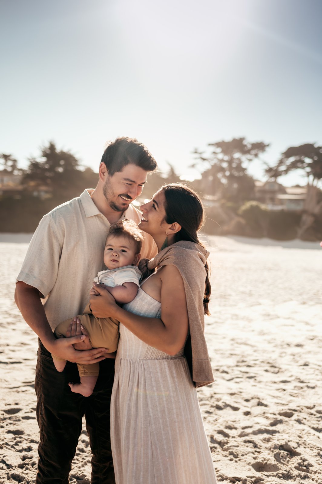 Parents nose to nose holding their baby boy in golden sunlight on Carmel Beach