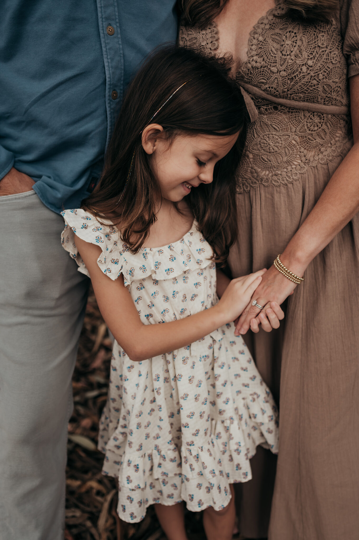 Little girl in a cream dress holding her parents' hands during a family session