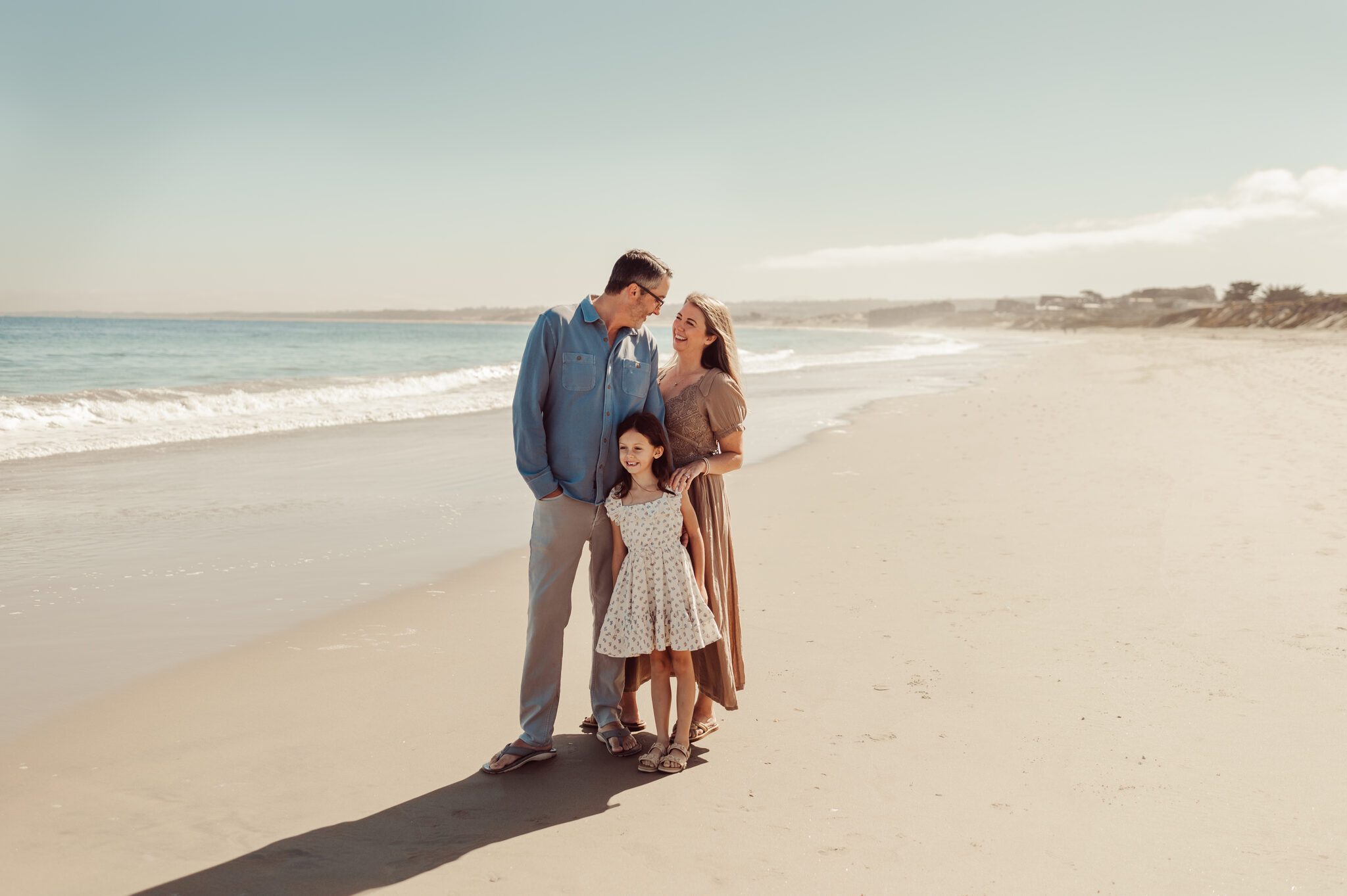 Parents and daughter huddled together at the shoreline of a Monterey beach