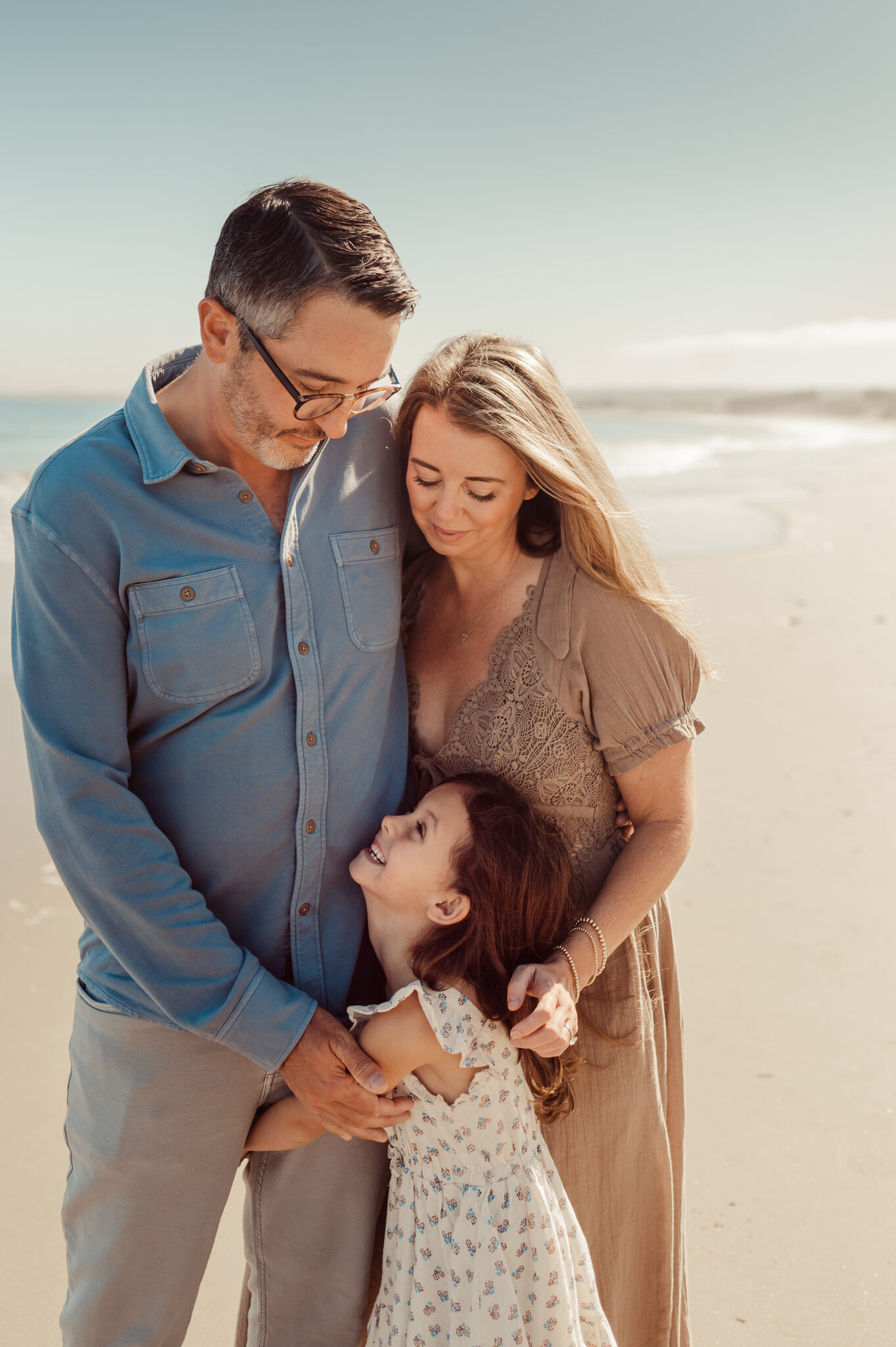 Mom and dad snuggling their daughter during a beach family session
