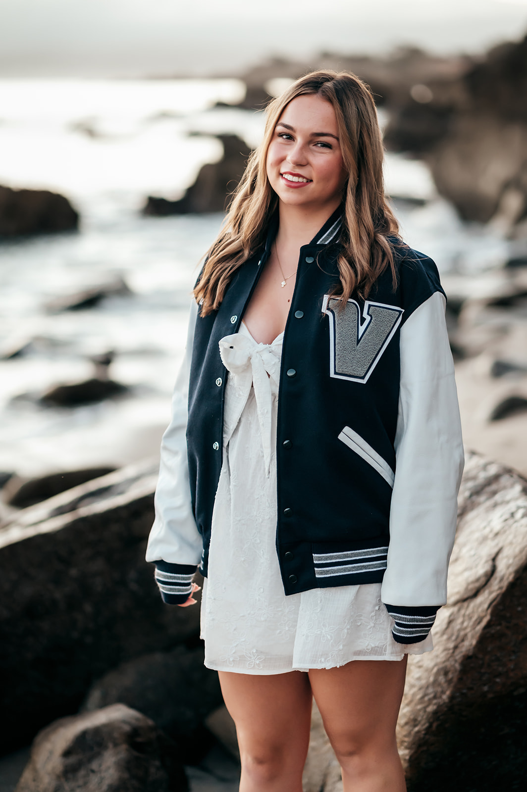 High school senior wearing her varsity letterman jacket with a V patch on the rocks at Lovers Point