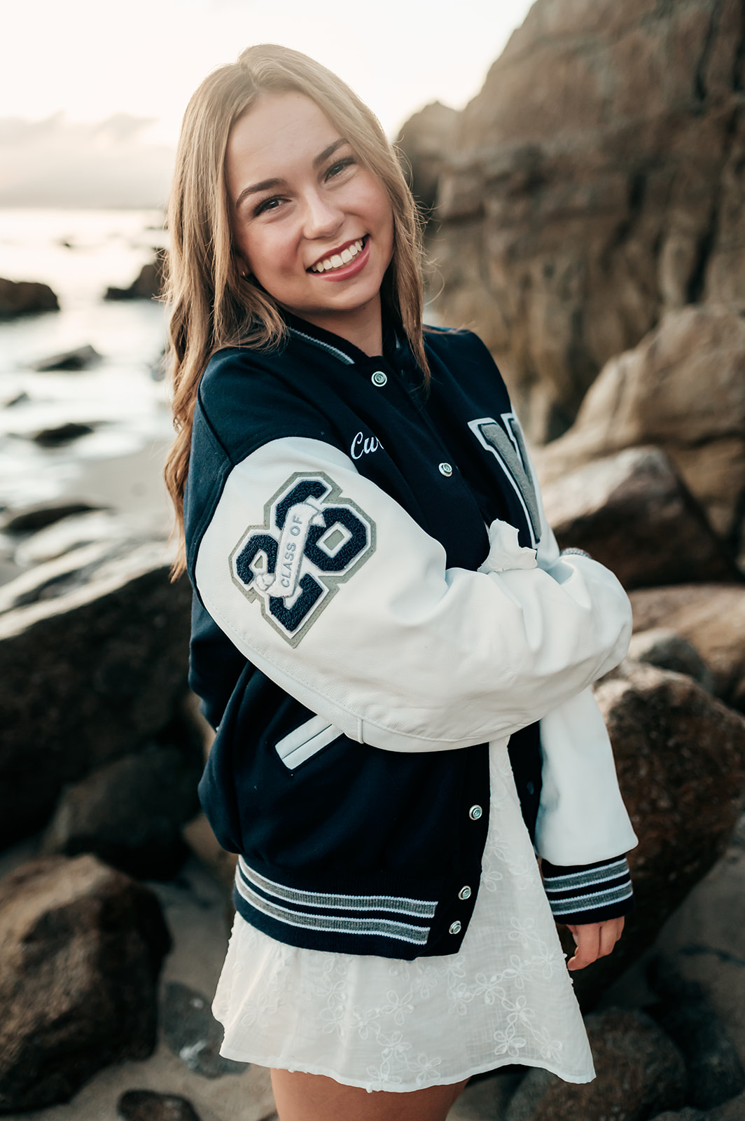 Senior grinning in her navy and white varsity jacket during her Pacific Grove senior session
