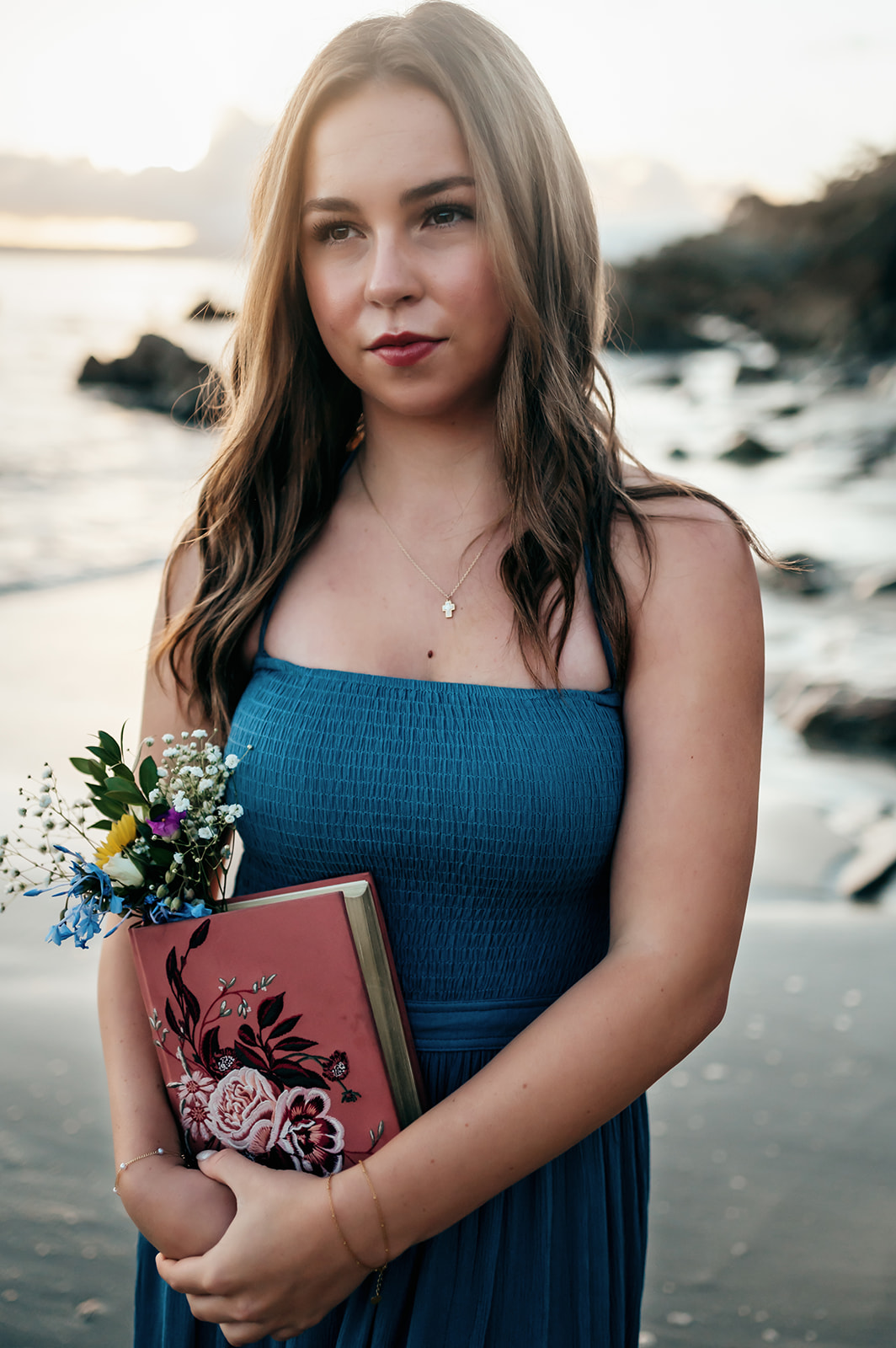 Senior holding her floral-covered Bible and a wildflower bouquet at her beach senior session