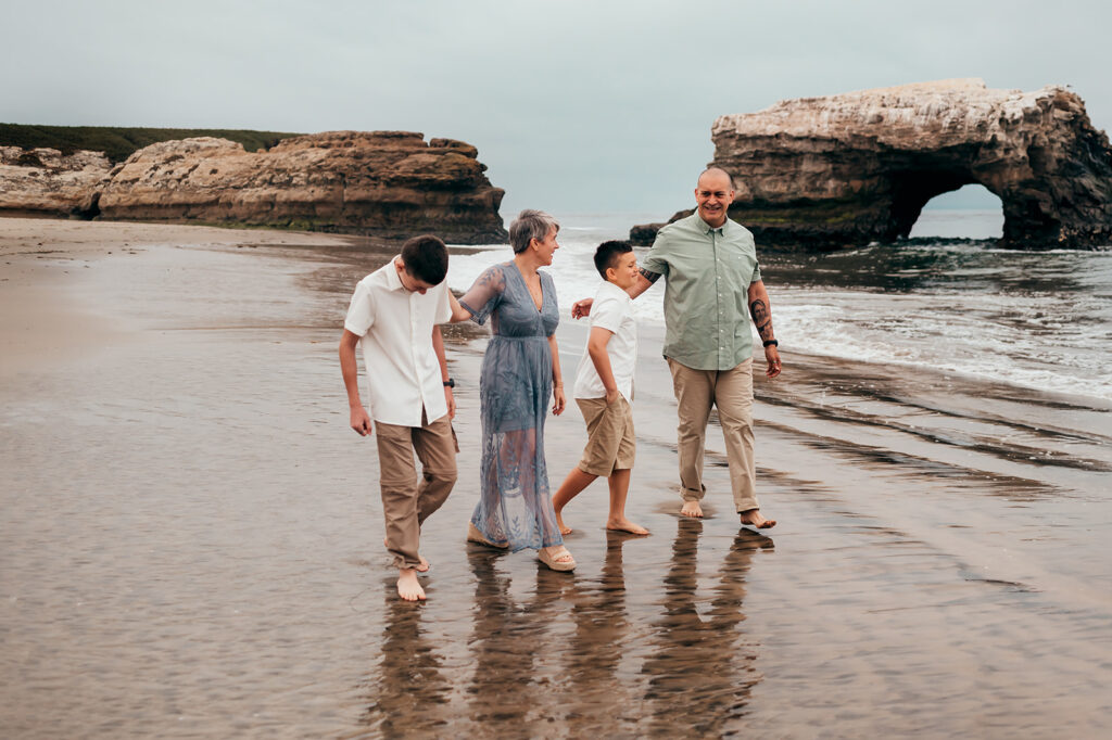 Mom, dad and two boys walking along the wet sand with their reflections at Natural Bridges State Beach
