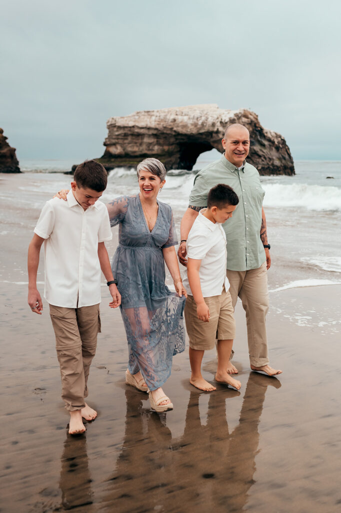 Family of four walking barefoot on the sand at Natural Bridges State Beach in Santa Cruz on a foggy morning