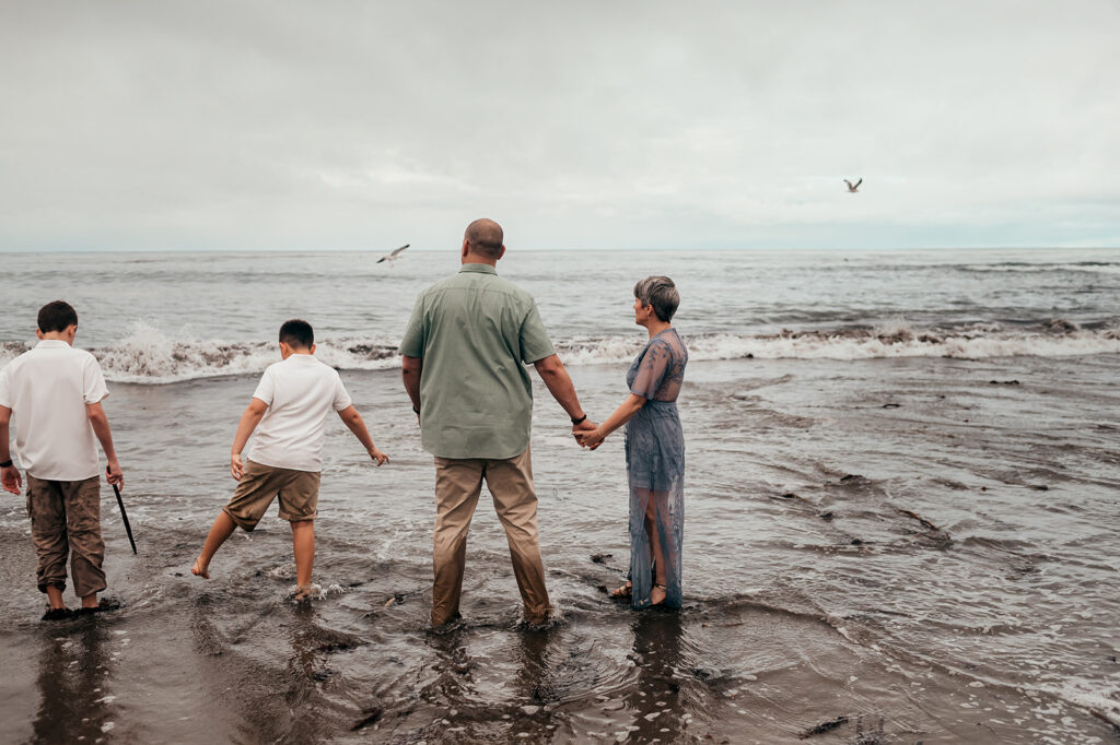 Family of four standing in the surf facing the ocean on an overcast morning in Santa Cruz, California