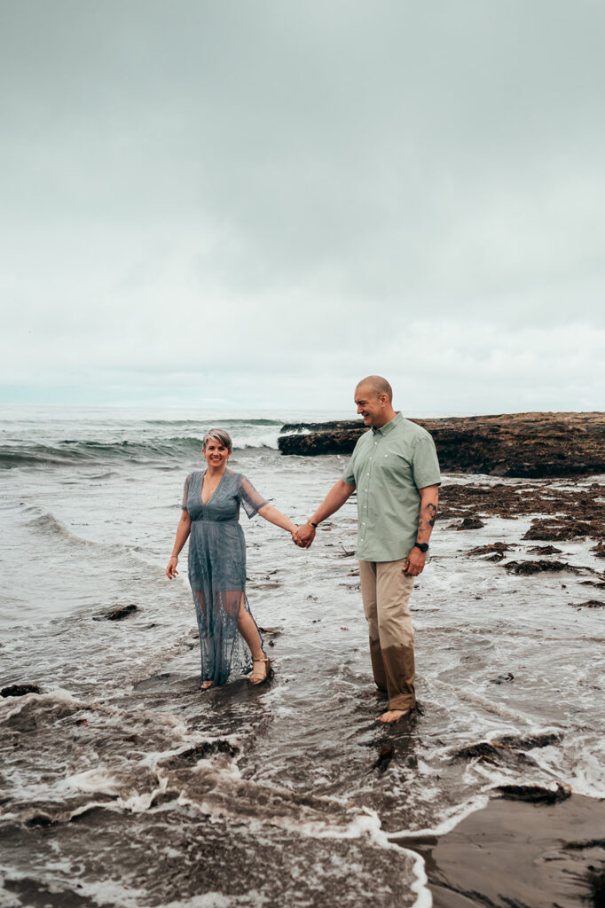 Couple laughing and holding hands in the shallow water at Natural Bridges State Beach in Santa Cruz