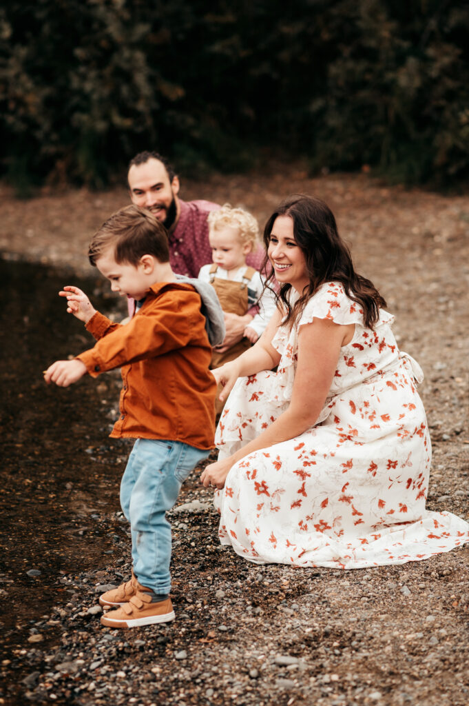 Family of four laughing together beside a creek during a fall family photo session, in rust and cream fall layers