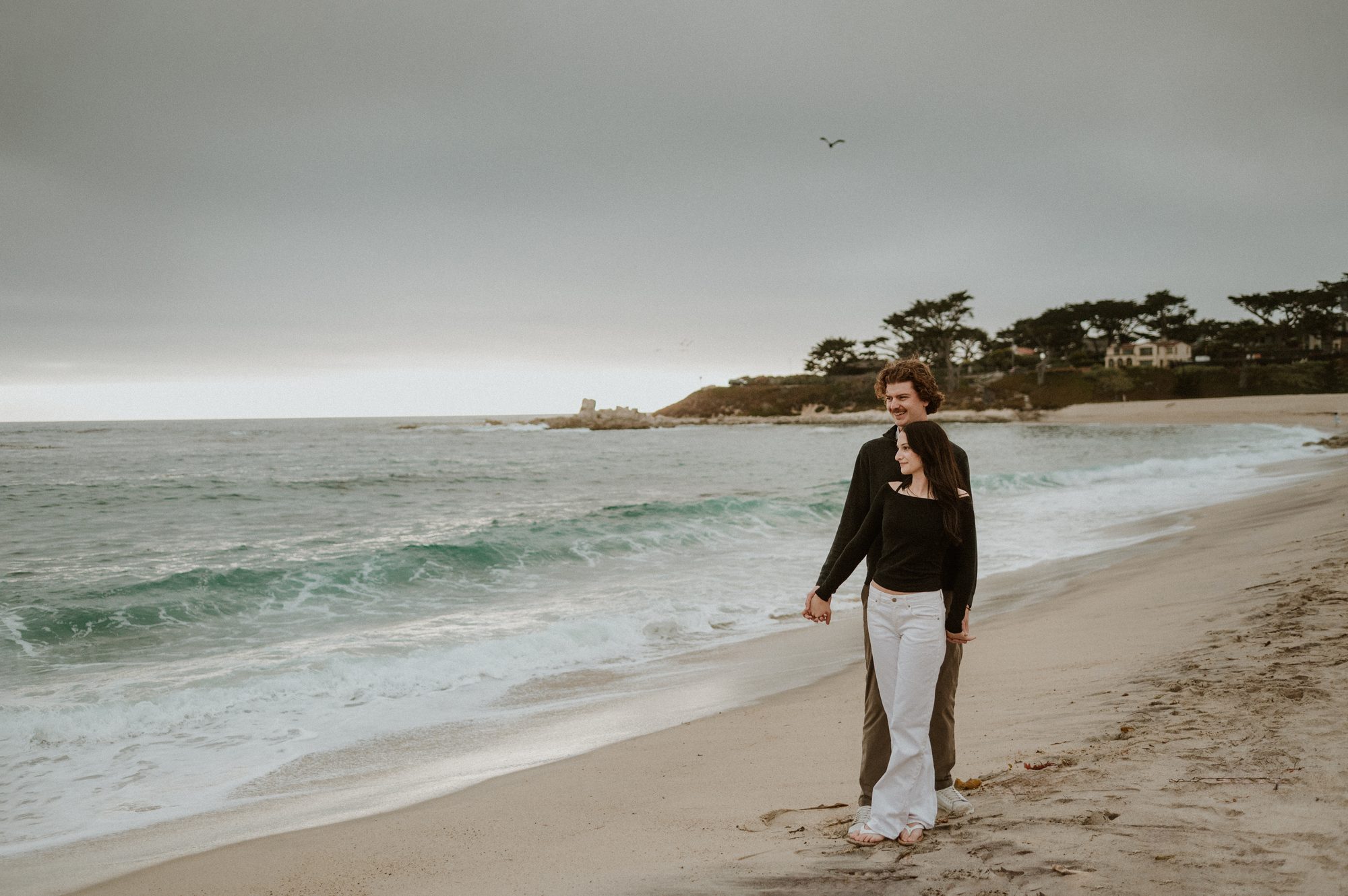 A couple walking at the water's edge on a foggy evening in Carmel-by-the-Sea
