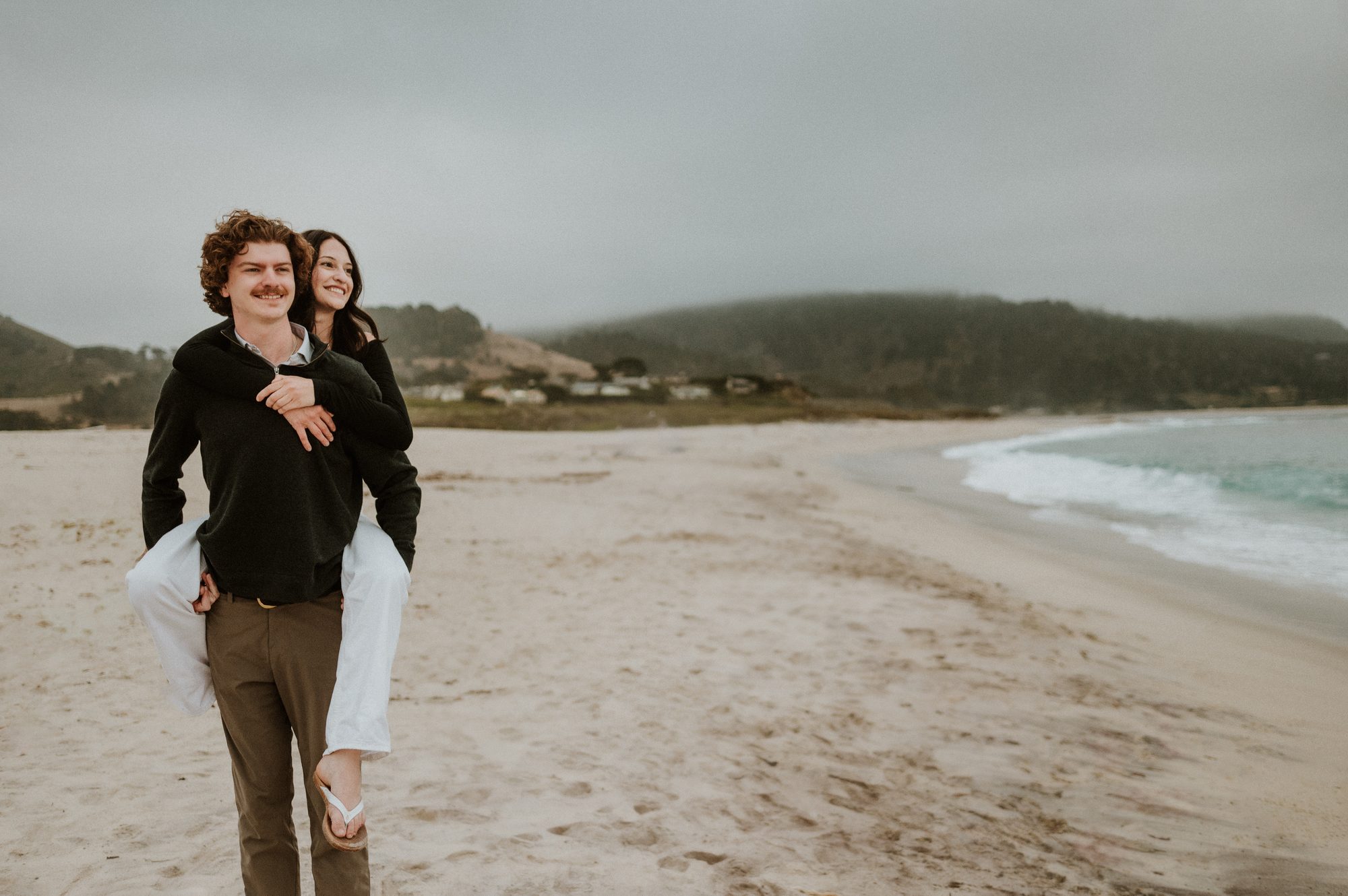 Two people laughing on the sand during an evening photo session in the fog