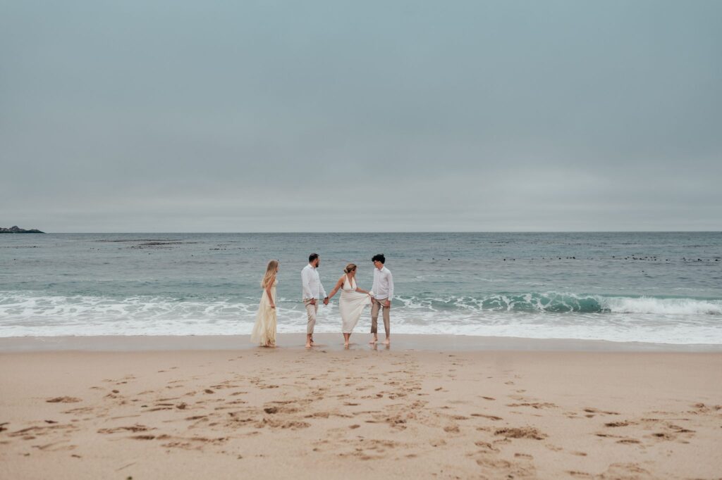 Mom, dad and their two teenagers walking into the shallow surf at Carmel River Beach in Carmel-by-the-Sea
