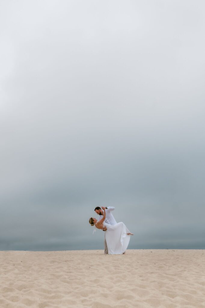 Couple dancing on the sand under a moody gray sky at Carmel River Beach