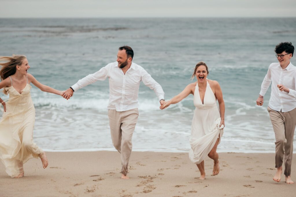 Family of four running barefoot and holding hands on the sand at Carmel River Beach at sunset