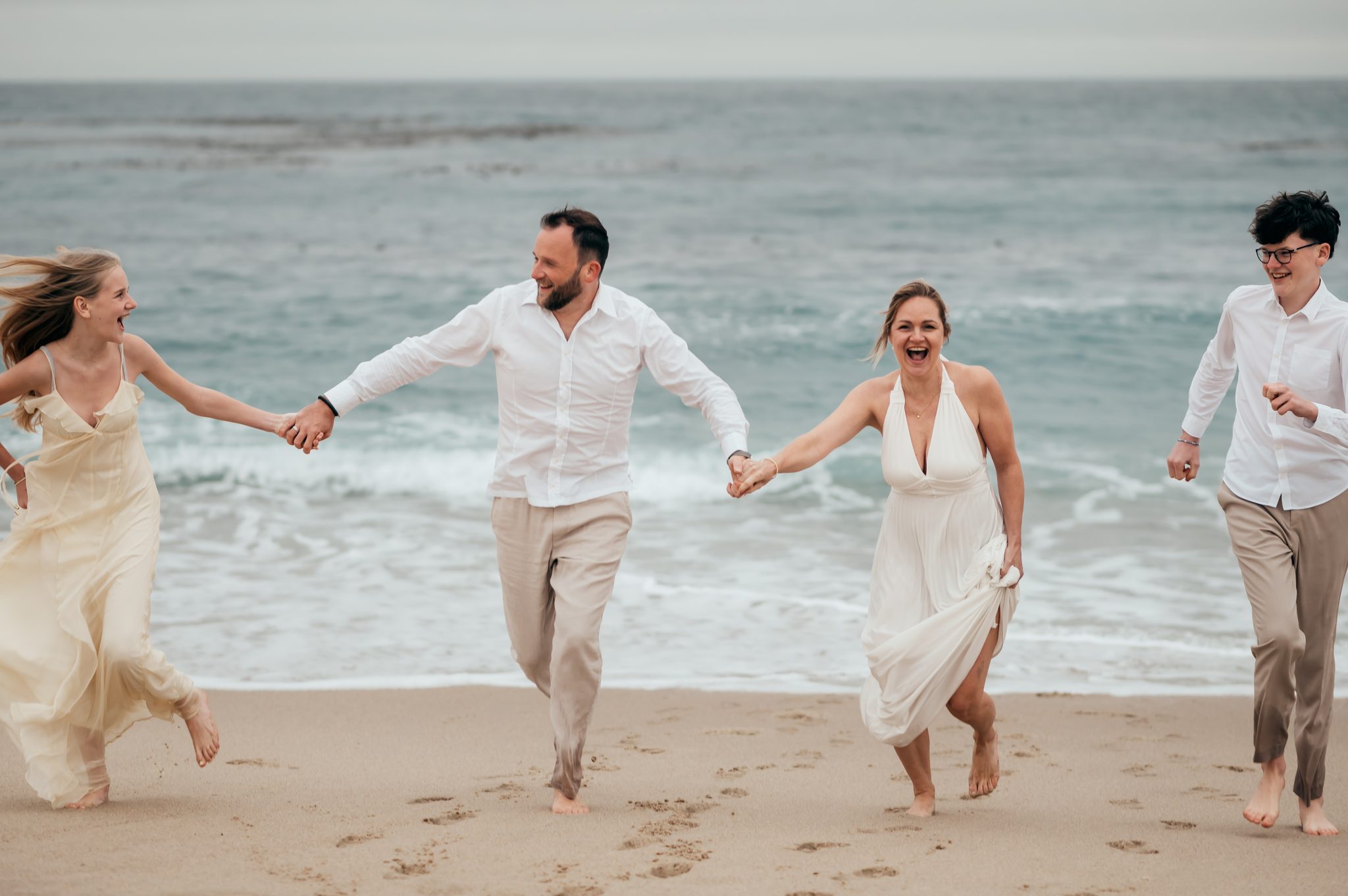 Family of four running barefoot and holding hands on the sand at Carmel River Beach at sunset