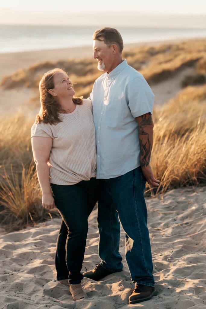 Mom and dad laughing together in the dune grass at Pajaro Dunes