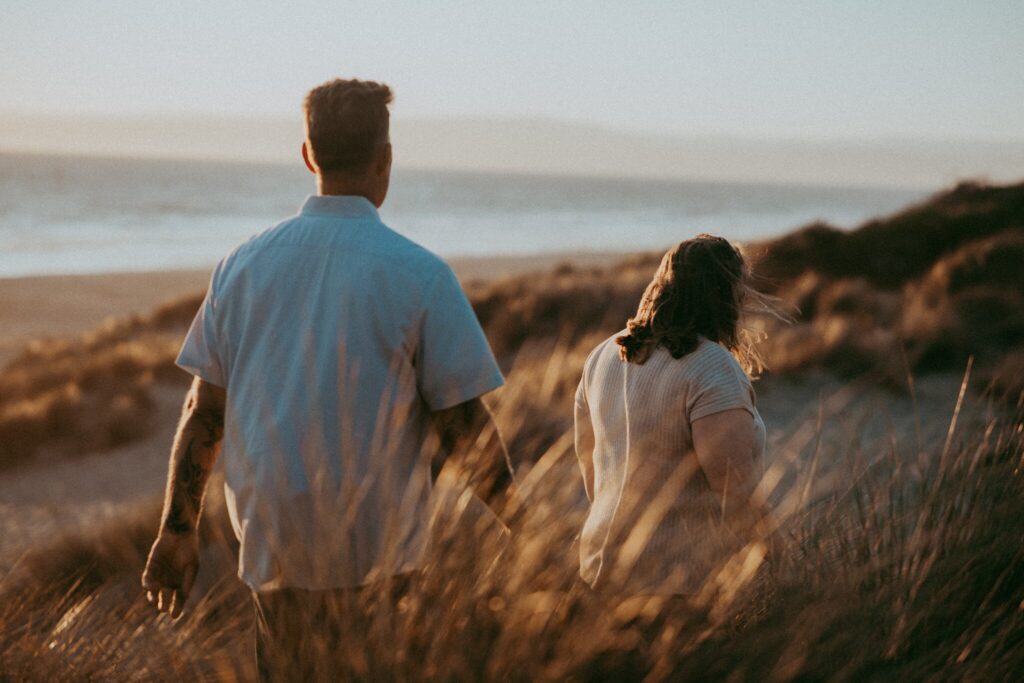 Mom and dad walking through the dune grass toward the ocean at Pajaro Dunes