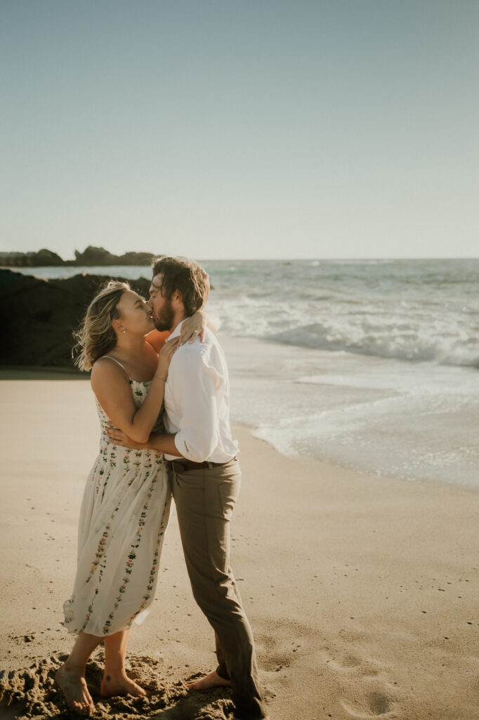 Nick and Patrycja kissing barefoot at the water's edge on Garrapata Beach in Big Sur