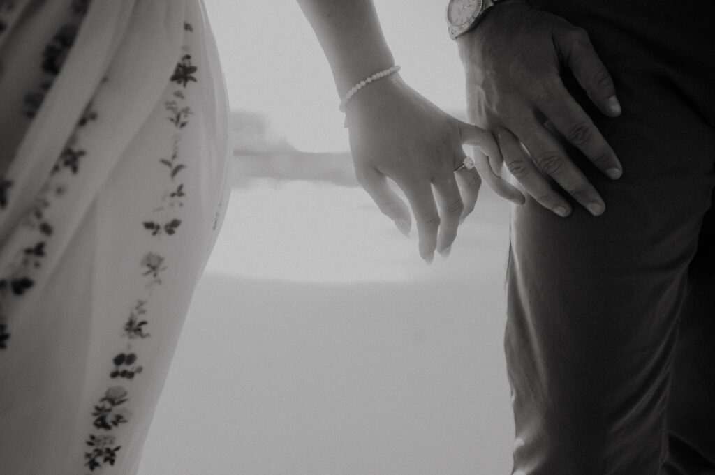 Black and white close-up of the engagement ring, Nick and Patrycja's hands touching on the beach