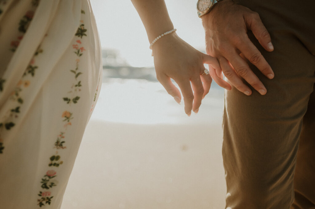 Close-up of Patrycja's engagement ring and pearl bracelet as she and Nick hold hands on the beach in Big Sur