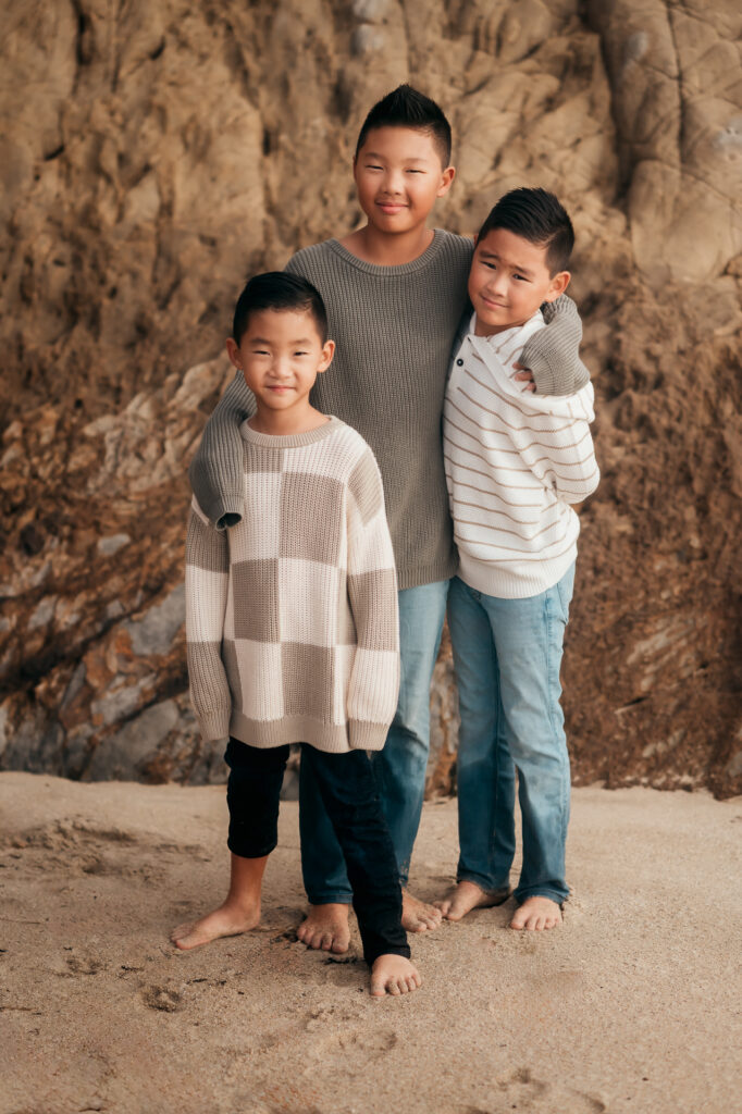 Three brothers in sweaters posing against a rock wall on a Big Sur beach