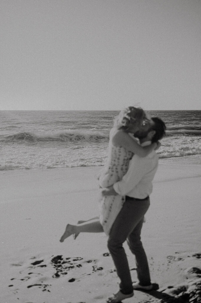 Black and white photo of Nick and Patrycja spinning and kissing on the beach at Garrapata