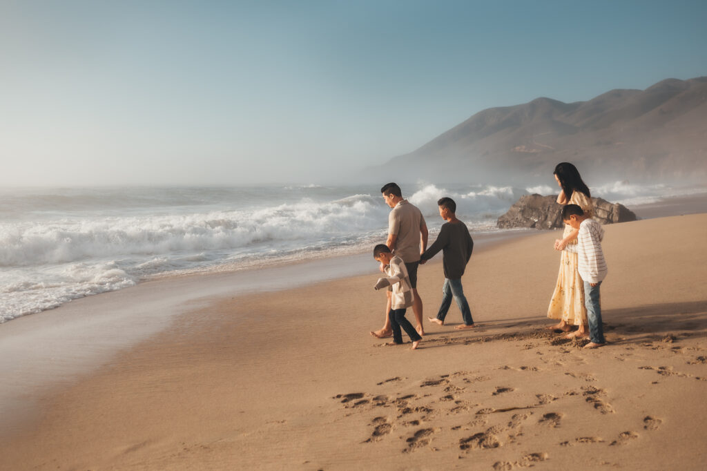 Family walking along the shoreline in sunshine with Big Sur hills behind