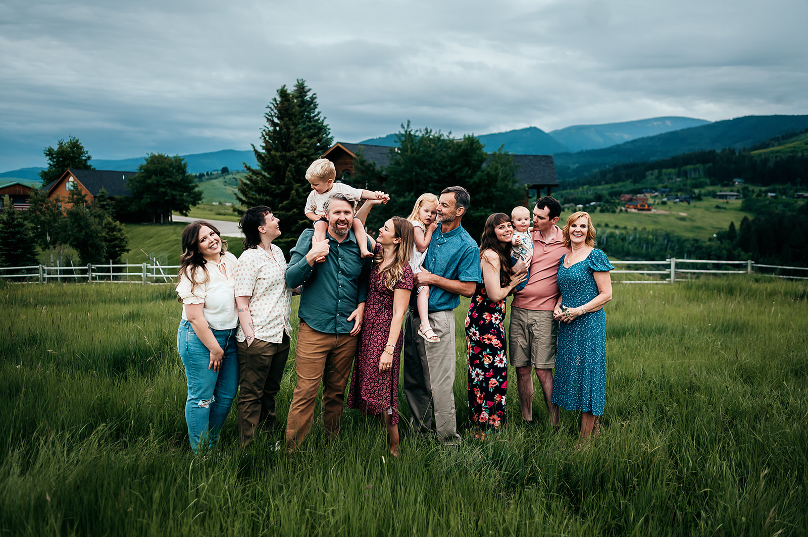 Twelve members of an extended family laughing together in a green mountain meadow, family photography by Britt Honey Photography
