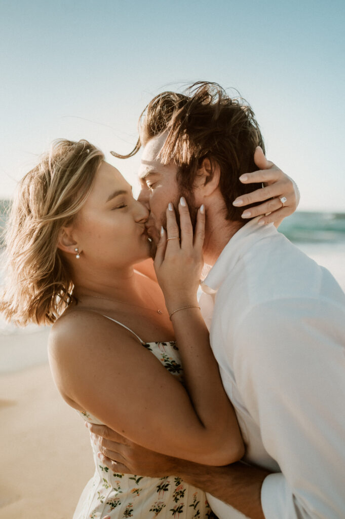 Nick and Patrycja kissing on Garrapata Beach at golden hour, her hands on his face