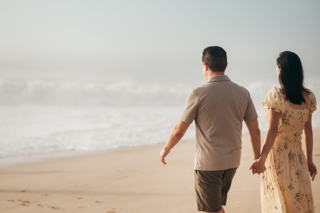 Parents holding hands walking toward foggy waves at Garrapata Beach