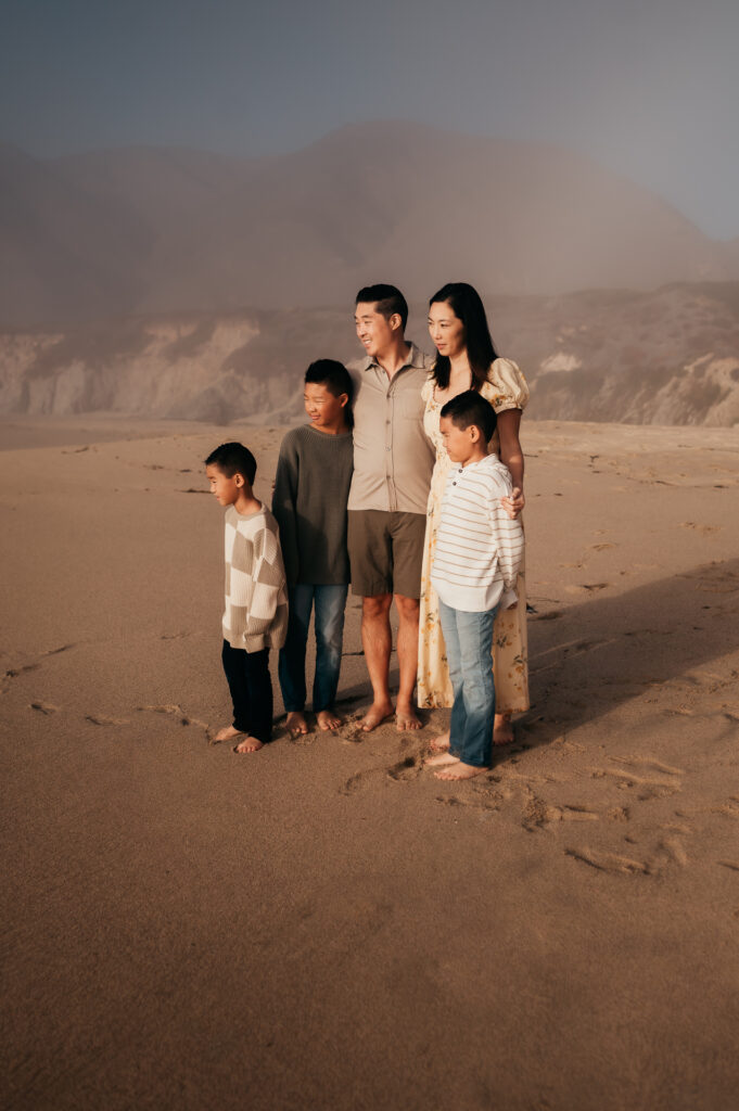 Family of five standing together on the sand as fog lifts at Garrapata