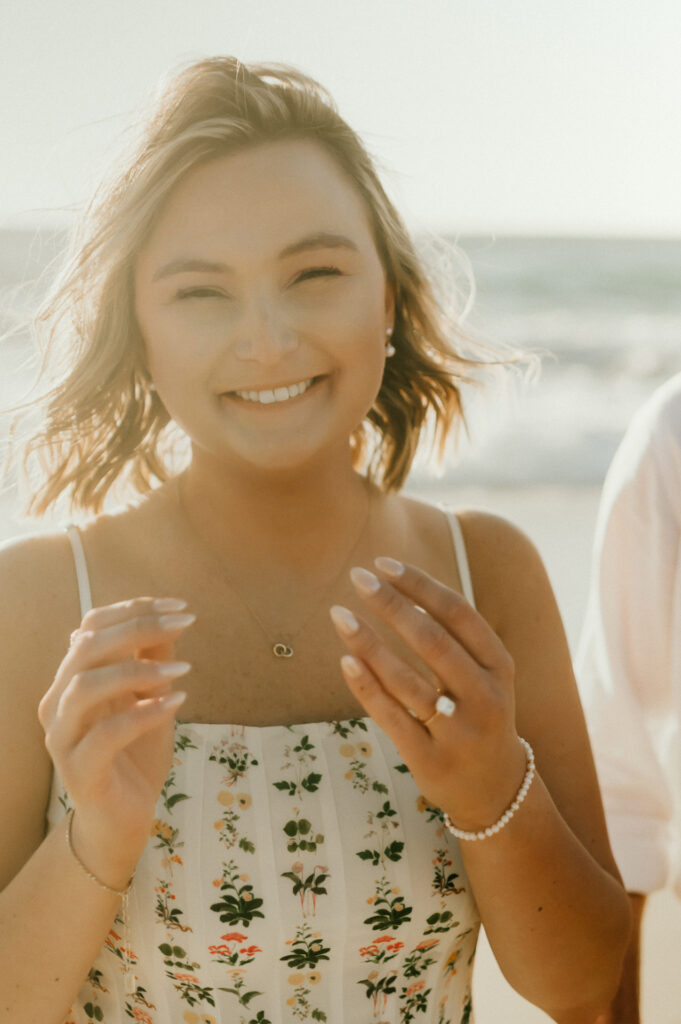 Patrycja smiling and showing off her engagement ring on Garrapata Beach with the ocean behind her
