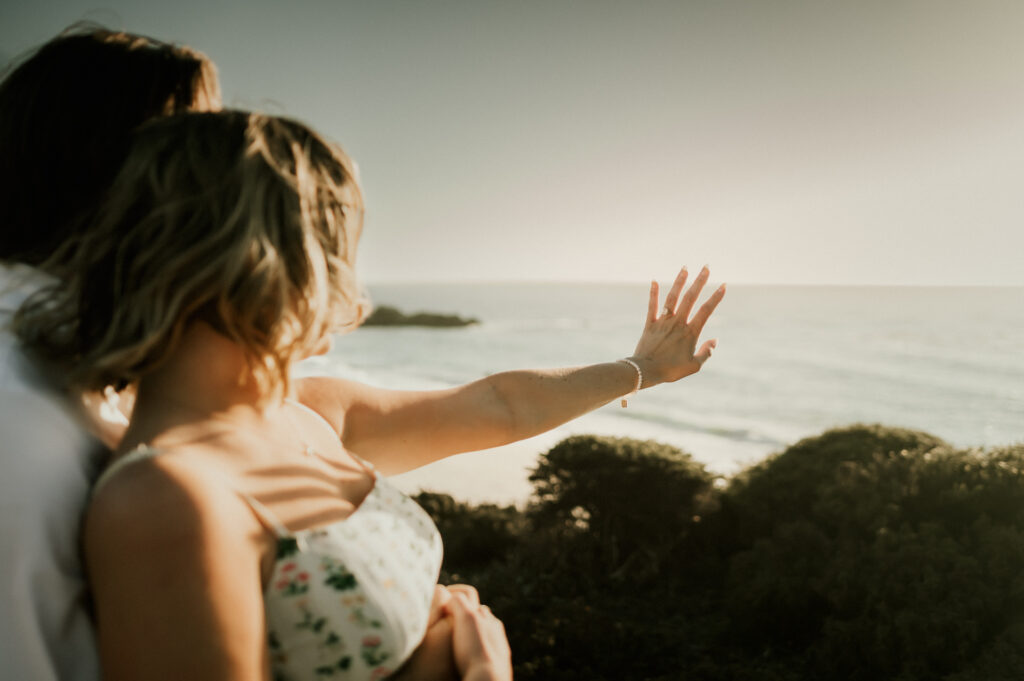 Patrycja holding out her hand to admire her new engagement ring with the ocean at Garrapata behind her