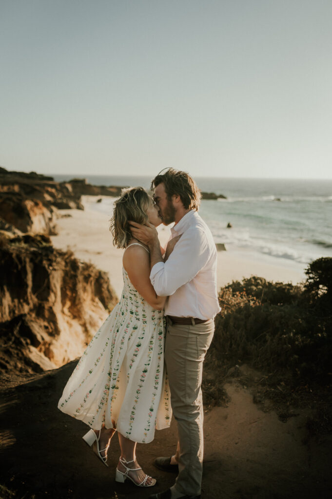 Nick and Patrycja kissing on the Garrapata cliffs right after the proposal, with the beach and Pacific Ocean below