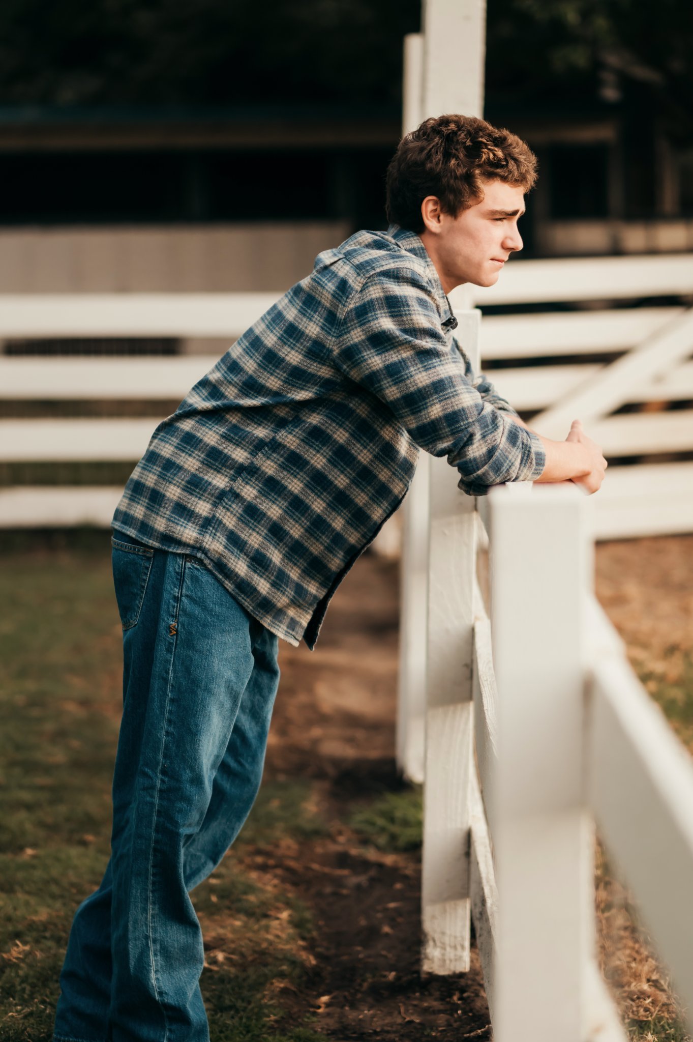 High school senior leaning over a white ranch fence in profile at sunset, Mission Ranch senior photos