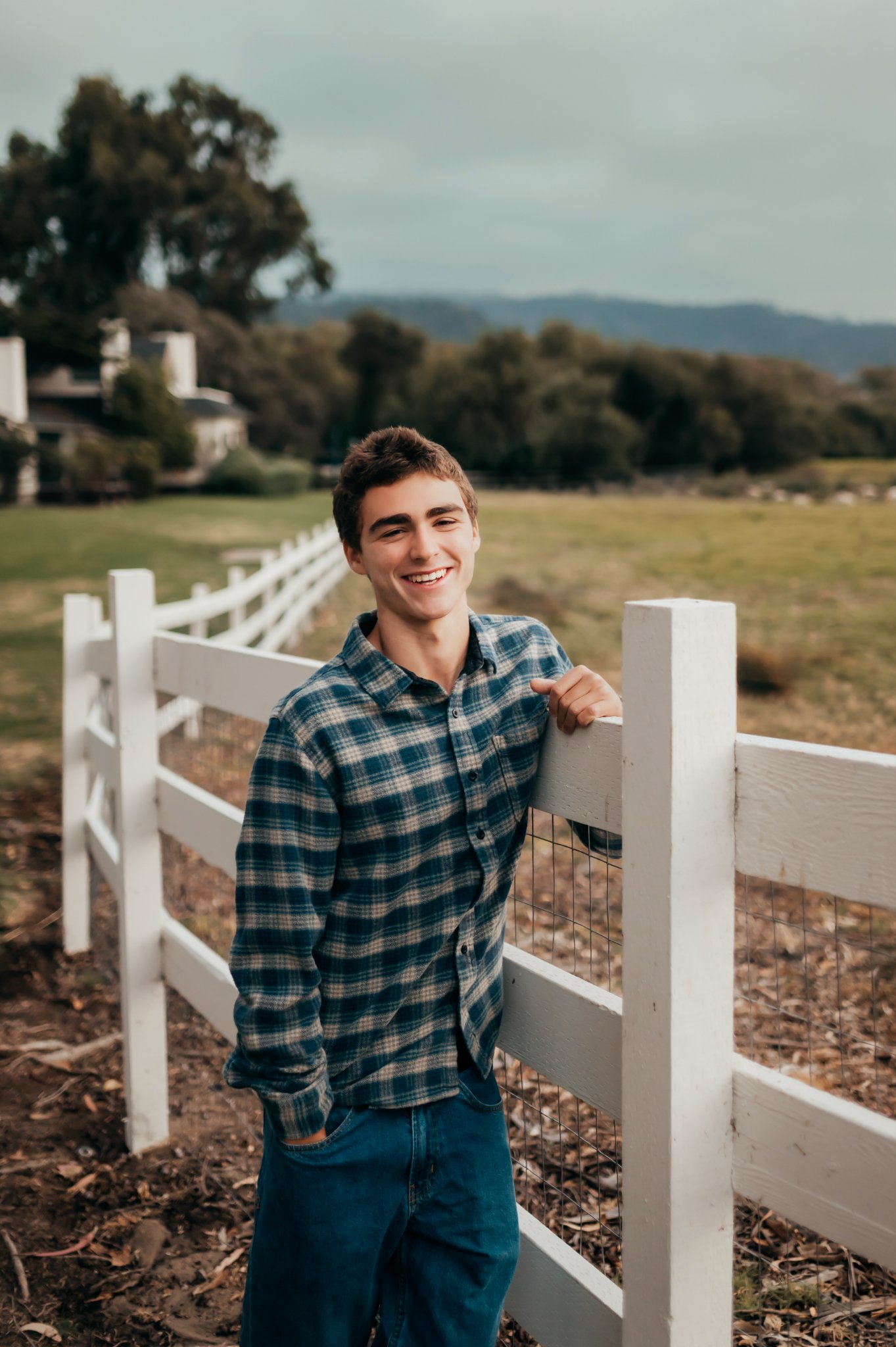 Smiling high school senior leaning on a white ranch fence at Mission Ranch in Carmel